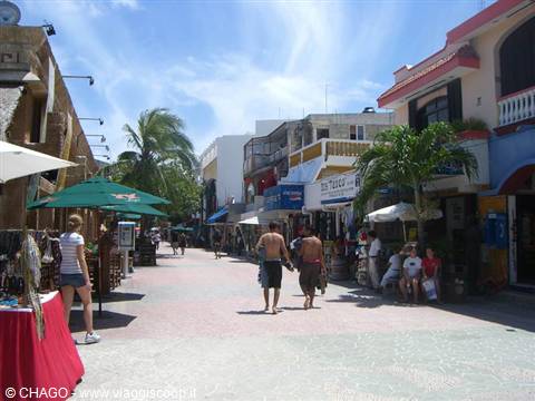 Tourists walking along Playa del Carmen's Quinta Avenida among shops and palm trees