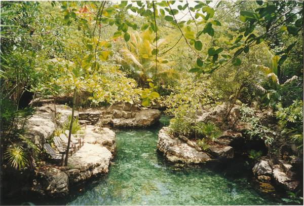 Lounge chairs on rocks beside an emerald river amid tropical jungle