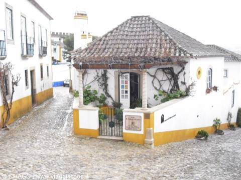 White house with arched entrance on cobbled street, looks like Óbidos