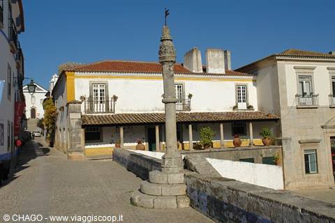 Ancient stone pillory in front of yellow and white houses in Óbidos