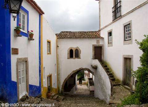 Whitewashed houses with blue bases and medieval arch over cobbled street in Óbidos