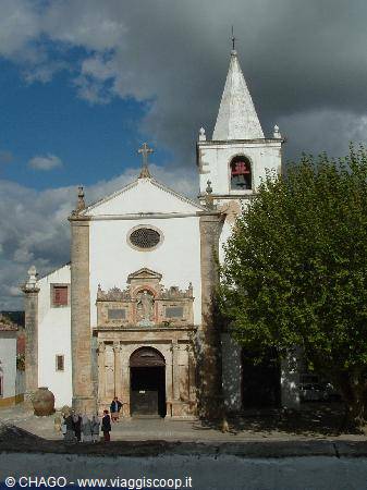 White church in Óbidos with bell tower and stone portal under clouds