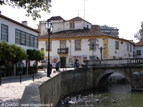 Old houses along the canal, stone bridge, people strolling and ducks in the water