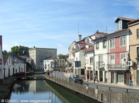 Canal between colorful houses and pedestrians in Aveiro, cars parked along the road