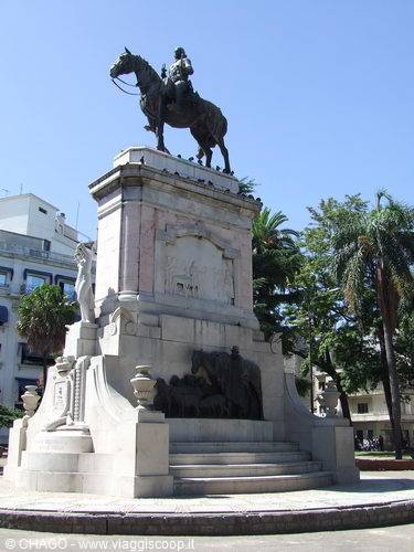Equestrian bronze statue on marble base in a tree-lined square
