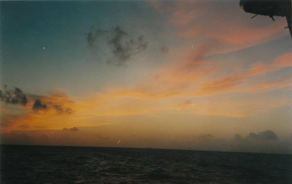 Orange and pink sky over dark sea, seen from a moving ship