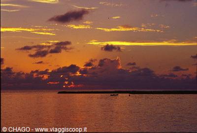 Golden clouds over calm ocean, a dark sand strip with a small boat