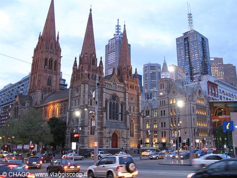 Sandstone Anglican cathedral among skyscrapers, city traffic at dusk