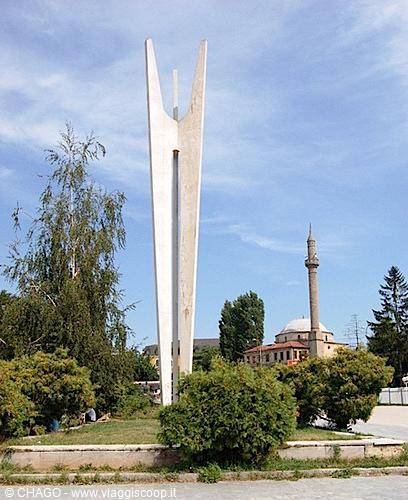 White concrete monument in a park, mosque with minaret in the background