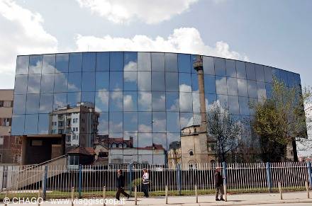 Mirrored glass facade reflecting a minaret and clouds, pedestrians walking by