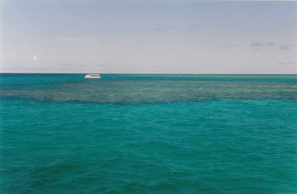 White boat on turquoise water, coral reef visible beneath the pale sky