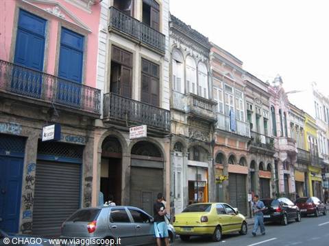 Colorful colonial buildings with wrought-iron balconies, parked cars, pedestrians walking along the street