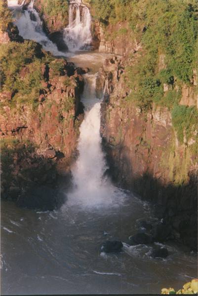 Waterfall plunging over brown rocks and green vegetation into the river below