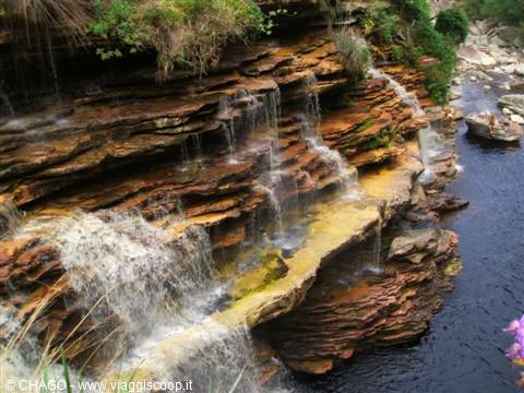 Small waterfalls cascade over orange sandstone rocks into a dark river