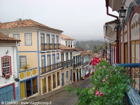 Cobbled downhill street lined with colorful colonial houses, red flowers in foreground, Ouro Preto