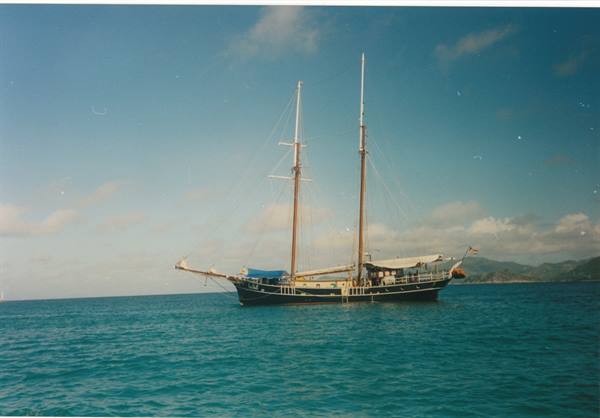Two-masted schooner anchored on turquoise sea, hills on the horizon