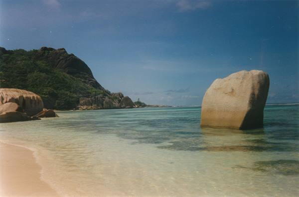 Granite boulder in turquoise water, pale sand and green hill behind