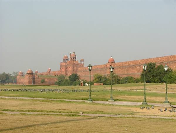 Red walls of Delhi's Red Fort with chhatris, pigeons and lampposts on the lawn