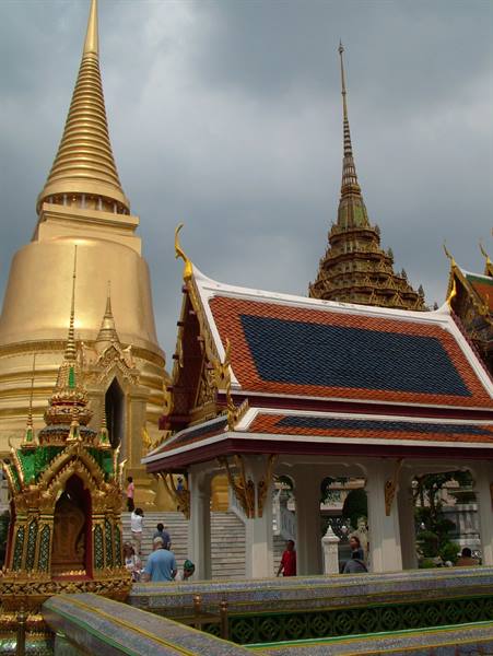 Golden stupa and white-roofed pavilion at Bangkok Grand Palace under grey sky