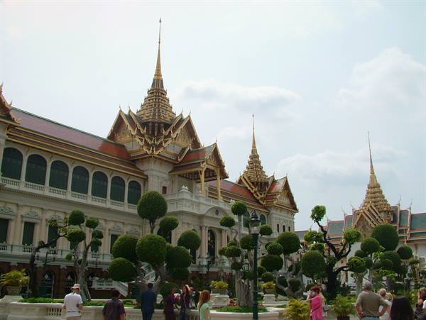 Tourists in the Grand Palace gardens in Bangkok among golden spires and manicured trees