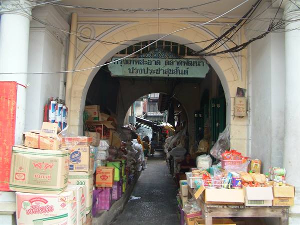 Colonial archway with Thai sign, boxes and goods crowd the market entrance