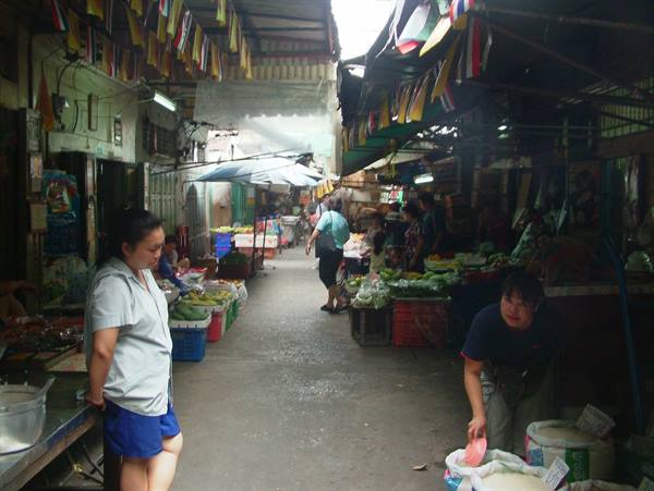 Covered market with vegetable stalls, colorful flags, woman serving rice