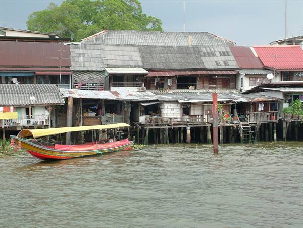Red longtail boat with yellow roof by stilt wooden houses on the river