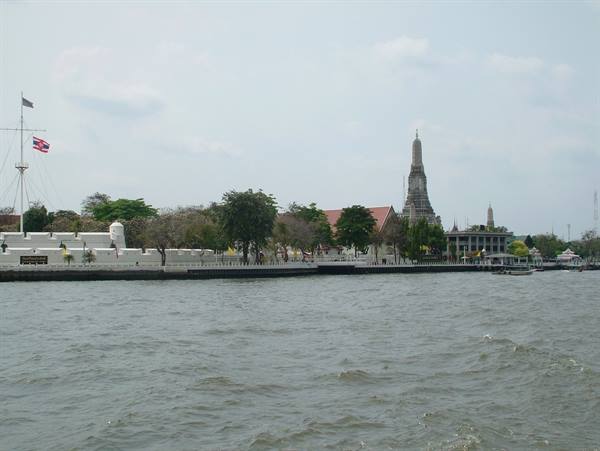 Wat Arun seen from the Chao Phraya river, white walls and spires under cloudy sky