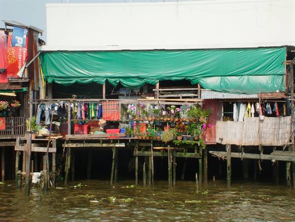 Wooden stilt house over the river, green tarps, hanging clothes and flower pots