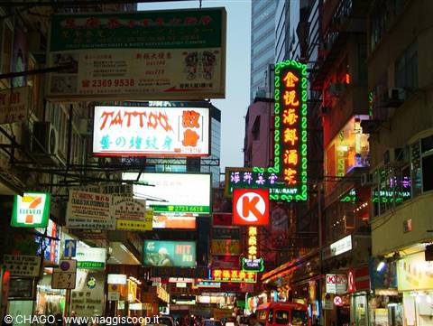 Neon signs crowding a busy Hong Kong street as evening lights switch on