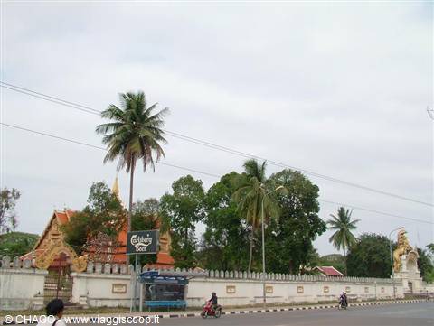 Motorbikes passing a white temple wall with palm trees in Vientiane