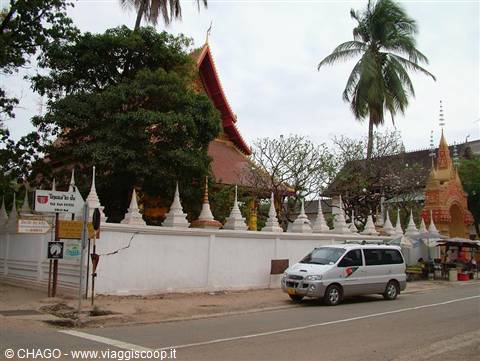 Temple with white wall and spires, palm trees, grey van parked on the road
