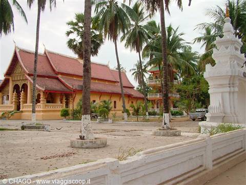Yellow temple with red roof among palms and white stupa in Vientiane