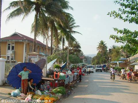 Street market under blue umbrella, palm trees, vegetable vendors and motorbikes along the road