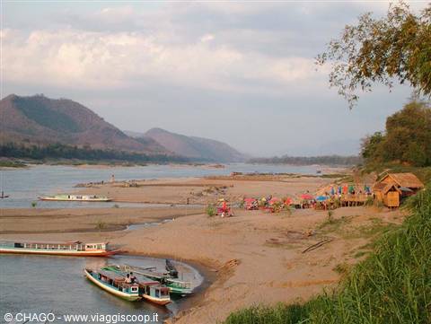 Wooden boats along the sandy Mekong riverbank, wooden stalls among the trees