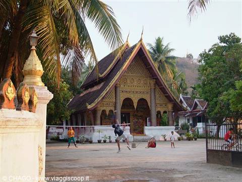Children play badminton in the courtyard of a golden wooden Buddhist temple
