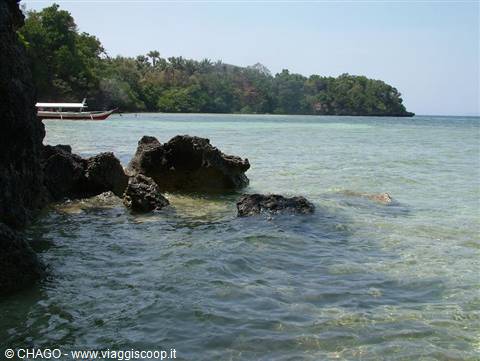 Red and white fishing boat by green coast, black rocks in clear water