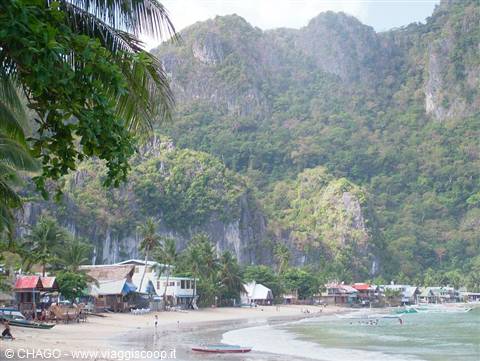 El Nido beach, boats on the sand and houses among palms beneath limestone cliffs