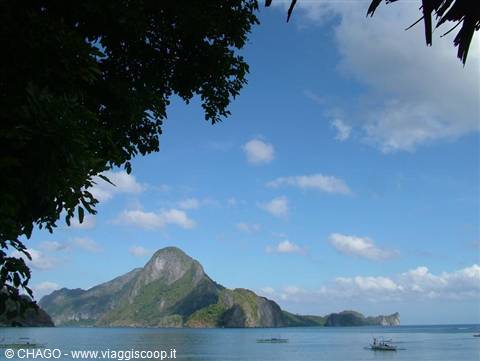 El Nido bay: limestone mountain over calm sea, boats and palm branches
