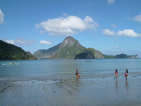 Children and boats on Corong Corong beach, limestone mountains of El Nido