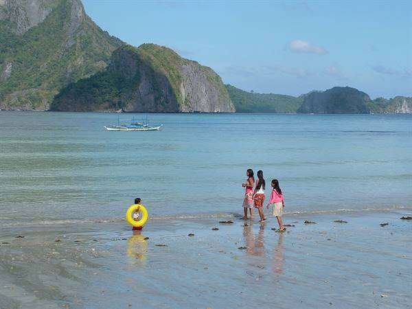 Children with yellow float on El Nido beach, boats beneath limestone cliffs