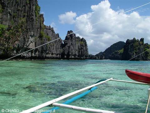 Outrigger boat bow on turquoise water among limestone karst cliffs