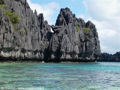 Tall dark limestone cliffs rise over clear turquoise water, El Nido
