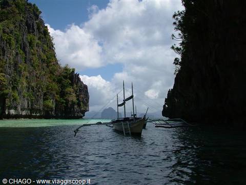 Wooden bangka boat between limestone cliffs in El Nido, turquoise water