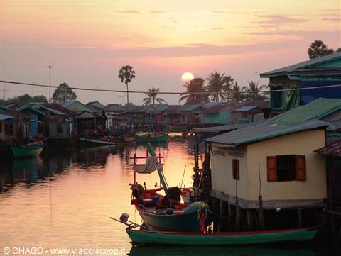 Boat moored beside stilt houses on pink reflecting water