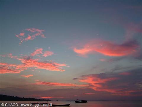 Fishing boats resting offshore beneath pink clouds at dusk