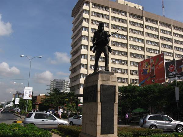 Bronze soldier statue on stone pedestal, traffic and skyscraper in Nairobi