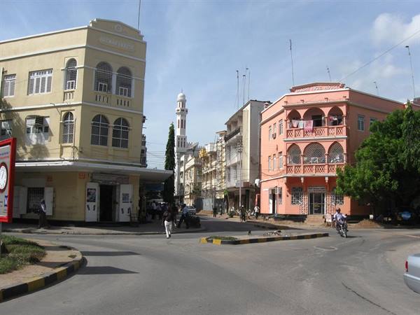 Intersection with yellow and pink colonial buildings, white minaret, pedestrians and motorcyclist