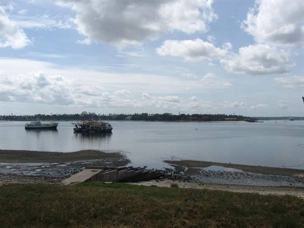 Boats moored on shallow water, concrete ramp, grassy foreground, cloudy sky