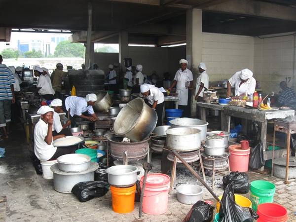 Cooks in white wash huge metal pots under a covered market